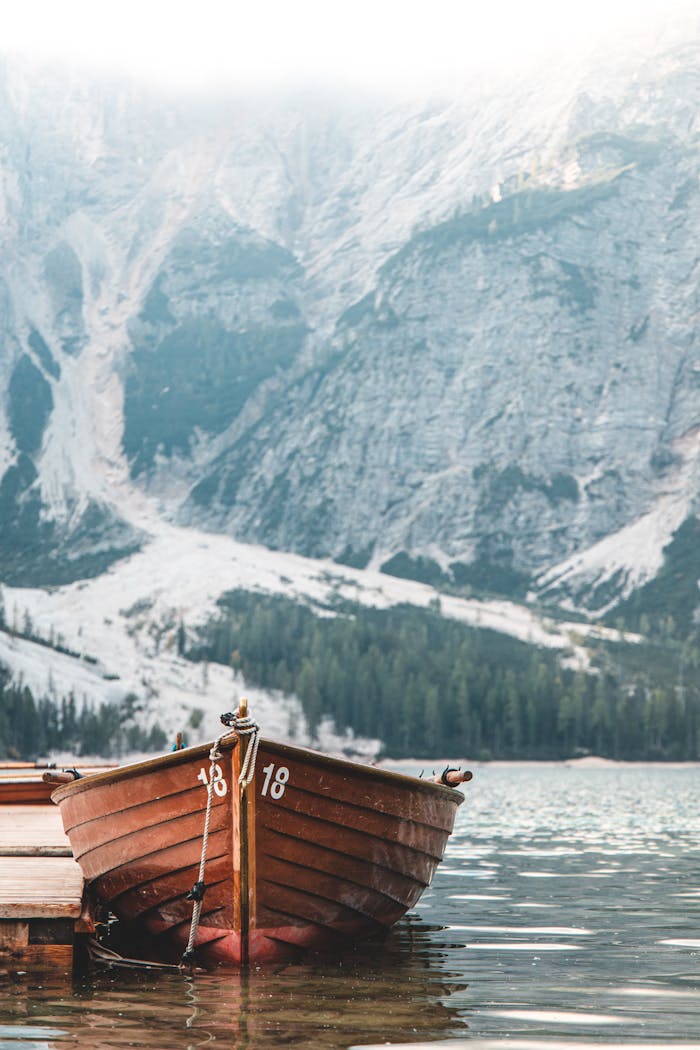 Serene scene with a wooden boat on an alpine lake surrounded by misty mountains.